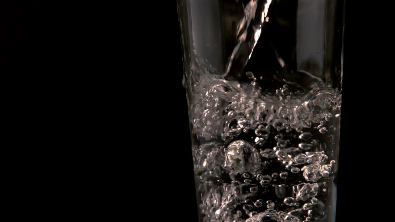 Acqua che si versa nel vetro su uno sfondo nero