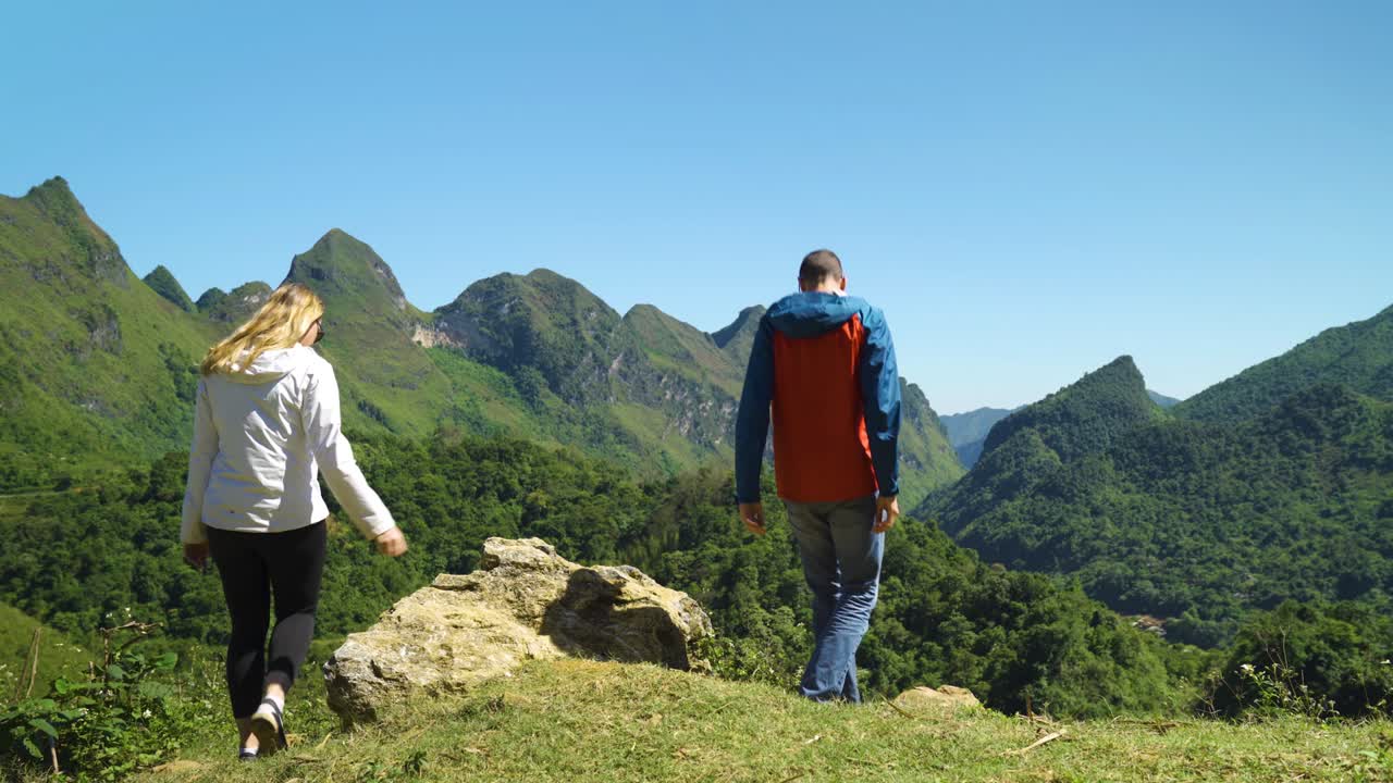 젊은 로맨틱 한 커플은 산꼭대기에서 휴식을 취하고 산책하고 앉아서 숨막히는 풍경을 바라보고 있습니다.