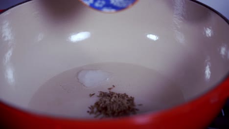 adding some cumin seeds to a pot of coconut oil to make fresh green papaya curry