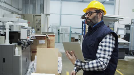 side view of serious engineer walking with laptop at factory