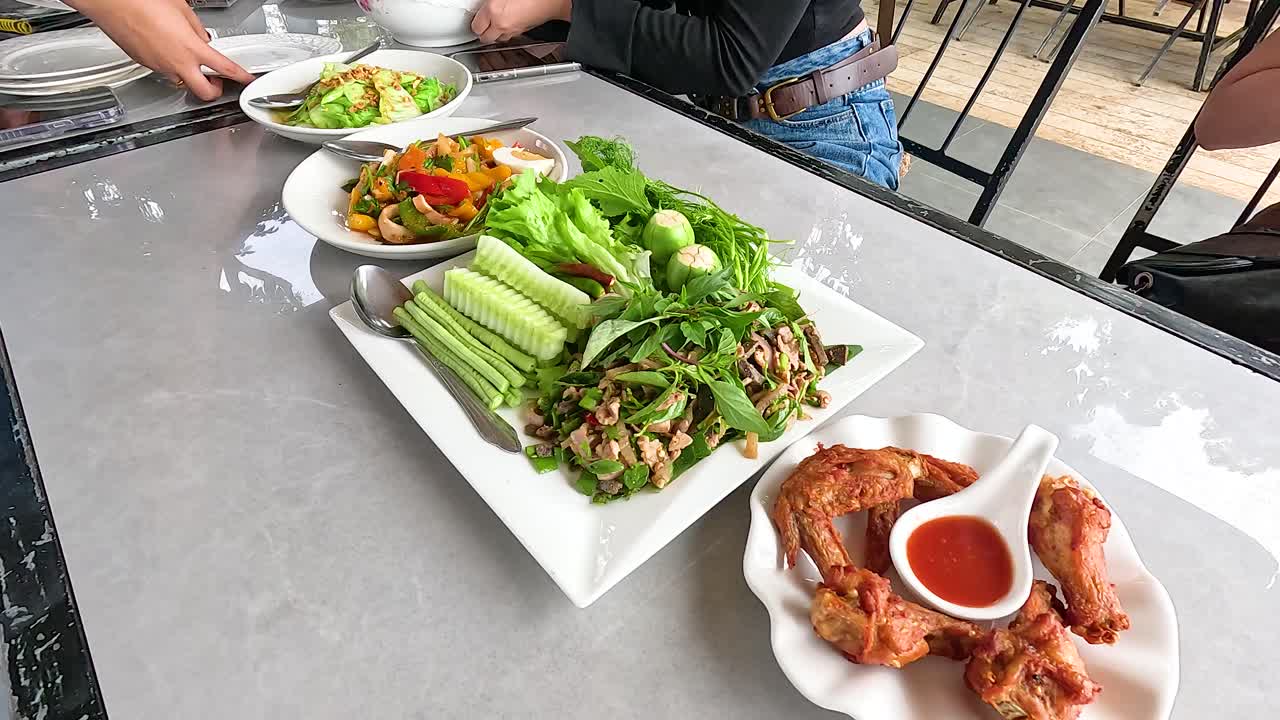 A table set with vibrant Laotian dishes, including fresh vegetables and grilled meats, in a casual outdoor setting