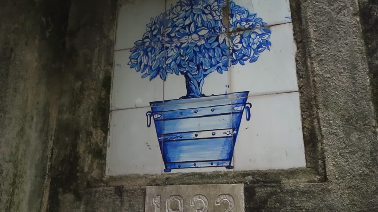 Primo piano di piastrelle azulejo di Lisbona usurate che mostrano un albero di agrumi in vaso dipinto di blu su un muro di pietra invecchiato con crepe e patina