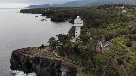 La-Maravillosa-Vista-Del-Faro-De-Kadowaki-En-Japón-Con-Una-Hermosa-Costa-Y-árboles-Verdes-Bajo-El-Cielo-Nublado---Toma-Aérea-Inclinada-Hacia-Arriba