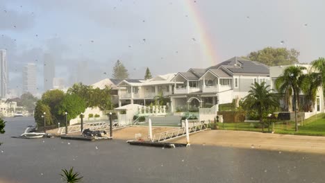 a serene gold coast canal scene with luxury homes, a sunshower, and a vibrant rainbow. soft lighting enhances the tranquil atmosphere