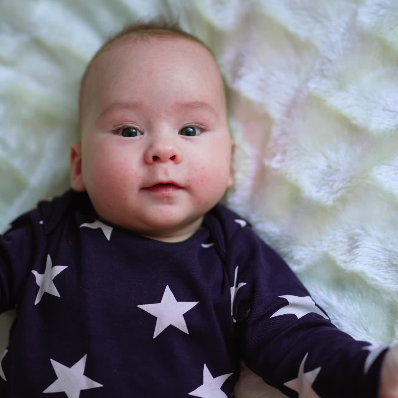 Happy cheerful healthy kid on the bed. Baby boy in dark sweater with stars on white backdrop. Close up. View from top