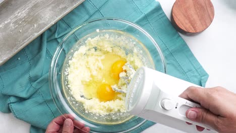 making a dessert called red raspberry tea cake made with fresh berries and vanilla buttercream frosting. great for tea parties. using a white electric hand mixer to beat in the farm fresh white eggs