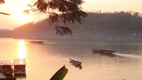 Resplandor-Dorado-Del-Atardecer-Reflejándose-En-El-Río-Mekong-Con-Barcos-Flotando-En-Luang-Prabang,-Laos,-Viajando-Por-El-Sudeste-Asiático