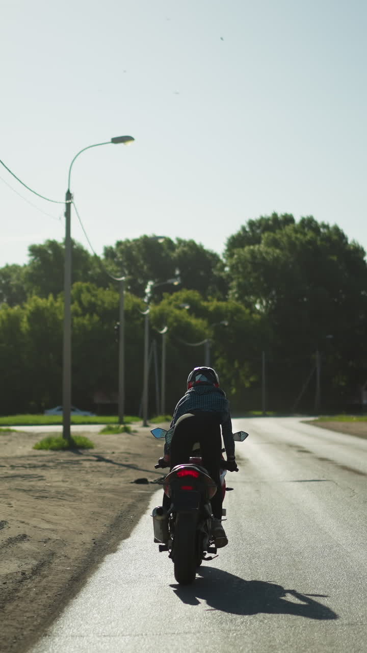 여성 자전거 타는 사람이 자전거를 타고 조용한 길을 달린다. 길은 나무, 전기 기둥, 주차된 자동차로 둘러싸여 있으며, 배경에는 건물이 보인다.