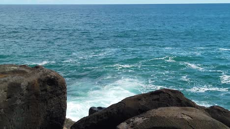 hd slow motion hawaii kauai static of ocean waves building and crashing with some ocean spray in right of frame with big lava rocks in foreground and ocean horizon at top of frame