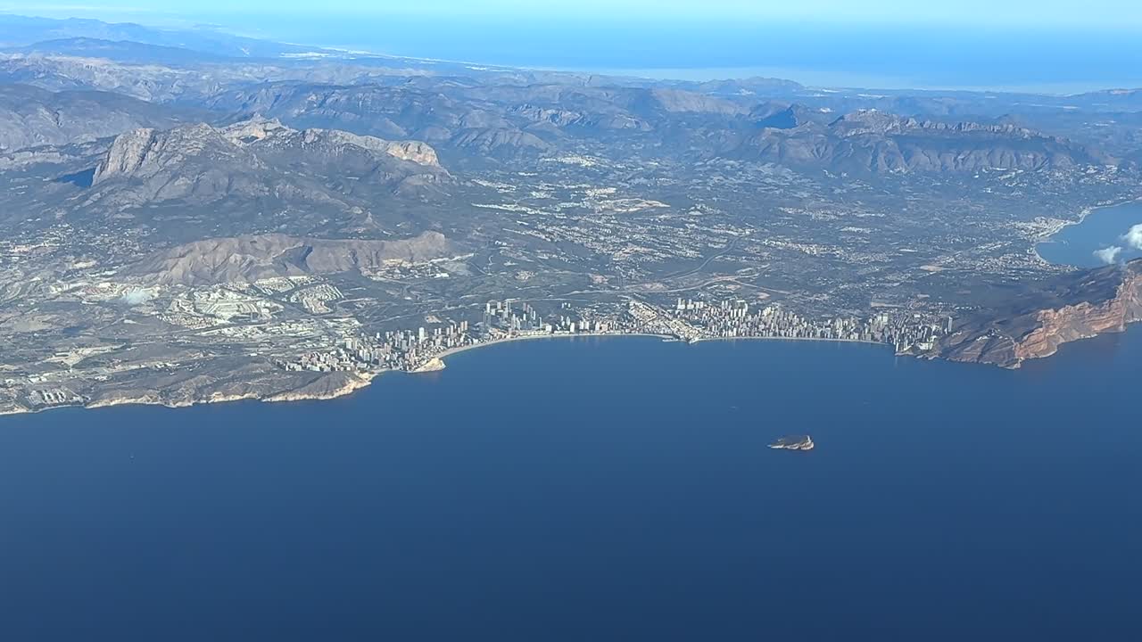 an elevated aerial side view of Benidorm city, in the Valencian coast, taken from a plane cockpit in a sunny summer morning. handheld camera shot
