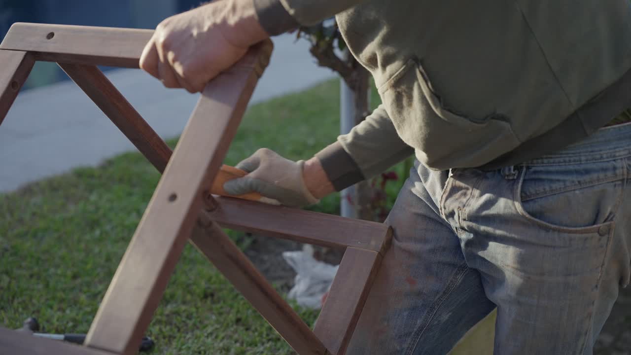 Worker Sanding Wooden Chair Frame with Electric Sander Outdoors on Grass