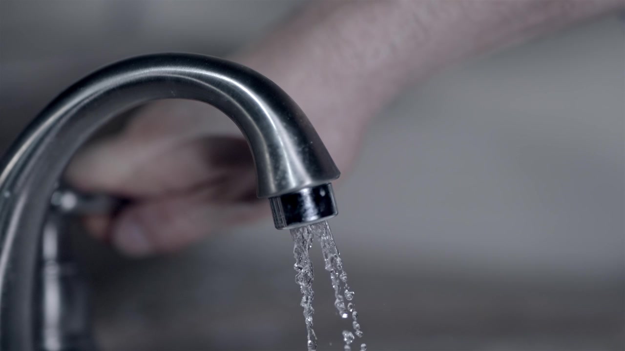 Blurred hand turning off the flowing water from a metal tap close up