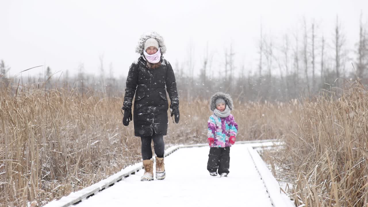 pretty mom and daughter walking in heavy snowstorm slomo