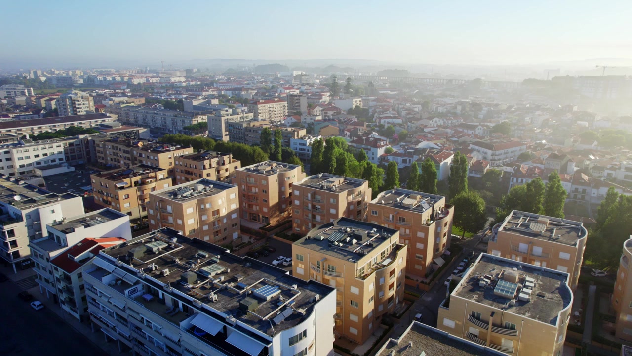Aerial 4K drone shot of a charming European city in the morning, featuring residential buildings, narrow streets, and a small green park bathed in soft sunlight.