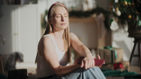 woman with eyes closed holding book at sun lit home during christmas