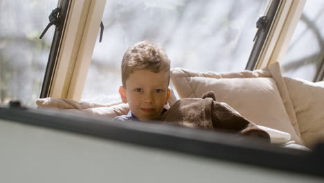 lindo niño acostado debajo de una manta en la cama de la caravana, mirando a la cámara y sonriendo