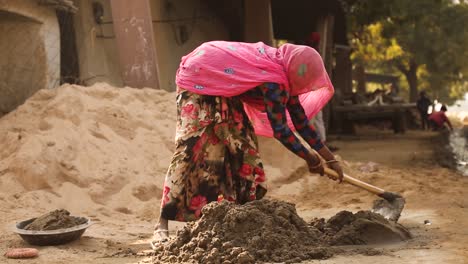 unrecognizable indian woman with head covered by pink veil kneading mortar or sand, tonk district in rajasthan