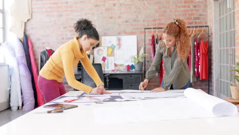 mujeres diseñadoras de moda felices y diversas discutiendo telas en el estudio, en cámara lenta