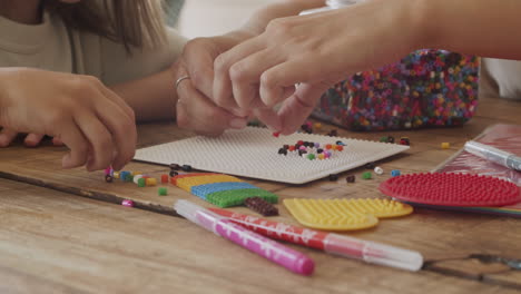 primer plano de las manos de una niña y su madre jugando con cuentas de colores