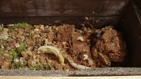 residuos alimentarios domésticos arrojados a un contenedor de compost de madera en el jardín, disparo deslizante