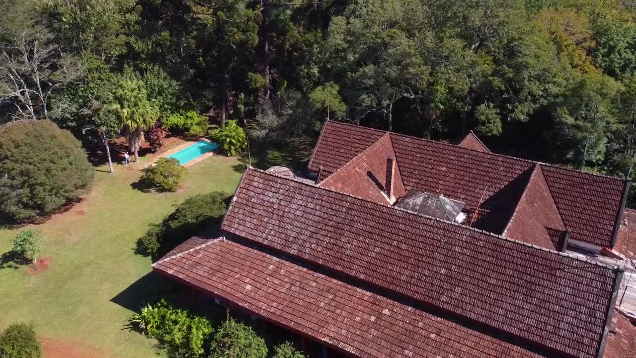 Stunning aerial view of a charming old house with red tiles and a triangular roof in Santa In&eacute;s, surrounded by lush green grass and tall trees, with a refreshing blue pool on the left