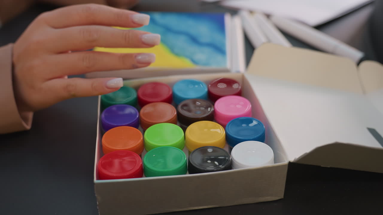 여성이 작은 바다 풍경 표면에 푸른색 페인트를 섬세하게 덧칠하여 캔버스 해변 풍경에 푸른 색조를 적용하고, 꼼꼼하게 푸른색 워시를 칠하고 있어요.