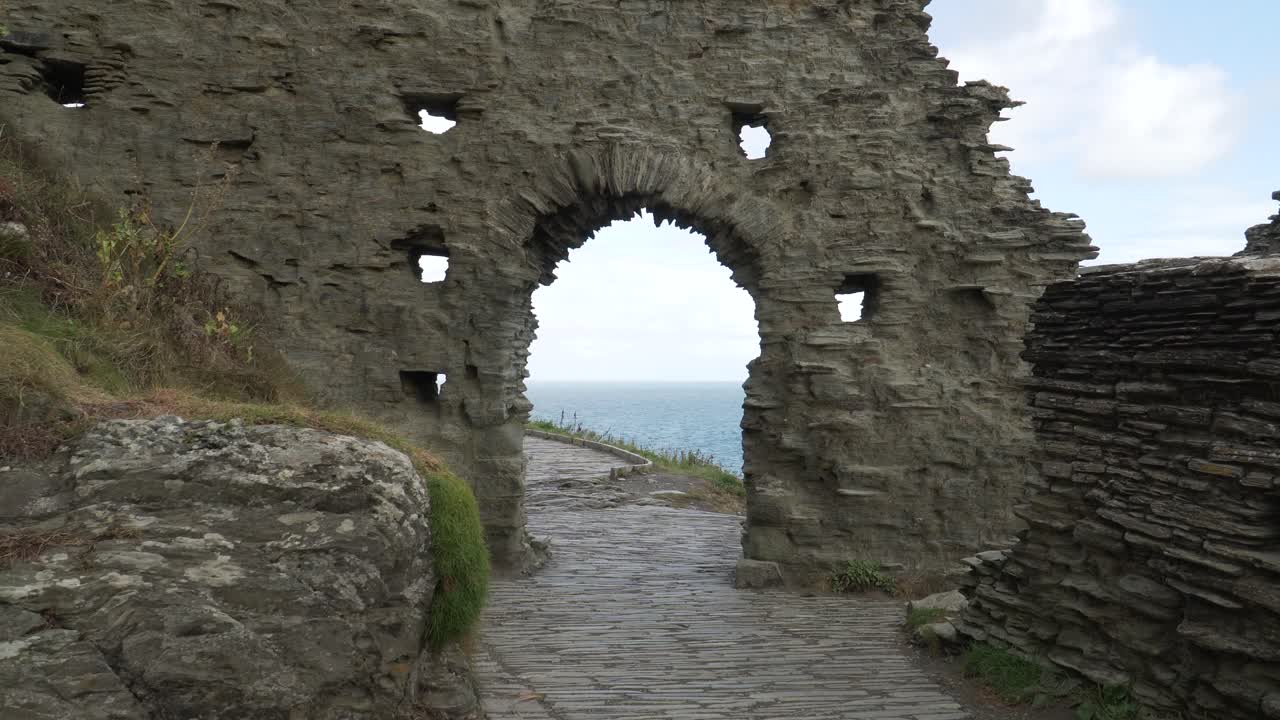 Close up view of one of the Tintagel Castle is a medieval fortification located on the peninsula of Tintagel, Cornwall. Medieval fortification wall ruins with an arched door showing the path and sea