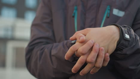 close-up of hands clasped tightly together in thoughtful contemplation, fingers interlocked with visible skin, set against blur background featuring urban buildings and soft natural light