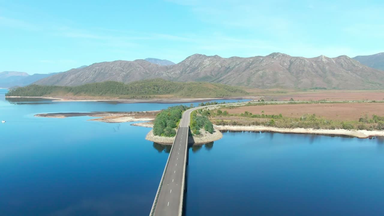 Flyover of a bridge over a lake in Tasmania with mountains in the distance