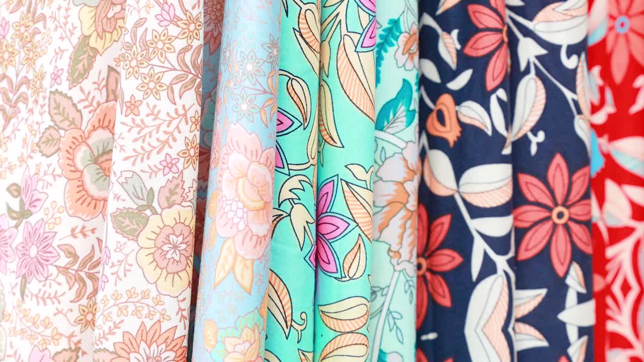 Colorful floral fabrics displayed in natural light, showcasing intricate designs and textures in a vibrant street market setting