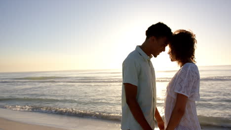 Una-Pareja-Birracial-Se-Encuentra-Cerca-De-Una-Playa-Al-Atardecer,-Con-Las-Frentes-Tocándose-Afectuosamente,-Con-Espacio-Para-Copiar