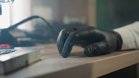 eine nahaufnahme der hand eines wissenschaftler mit handschuhen, die auf einem labortisch ruht, mit laboreinrichtungen im hintergrund sichtbar