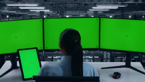 back view of asian woman working with tablet and multiple computer monitor with mock up green screen in data center