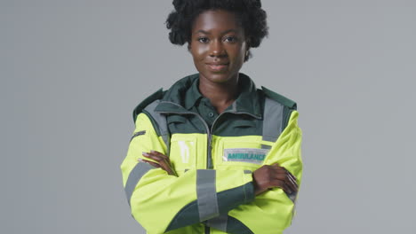 full length studio portrait of smiling young female paramedic in uniform against plain background