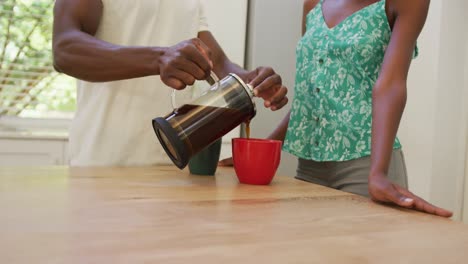 Mittelteil-Eines-Afroamerikanischen-Paares-In-Der-Küche,-Das-Kaffee-Aus-Der-Kaffeemaschine-Einschenkt