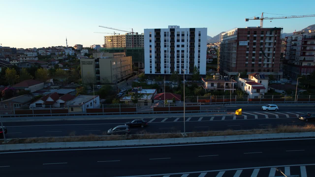 Highway lanes on Tirana city ring road at twilight with suburban buildings, traffic, people returning home