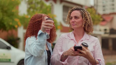two women talking and interacting with a smartphone outdoors