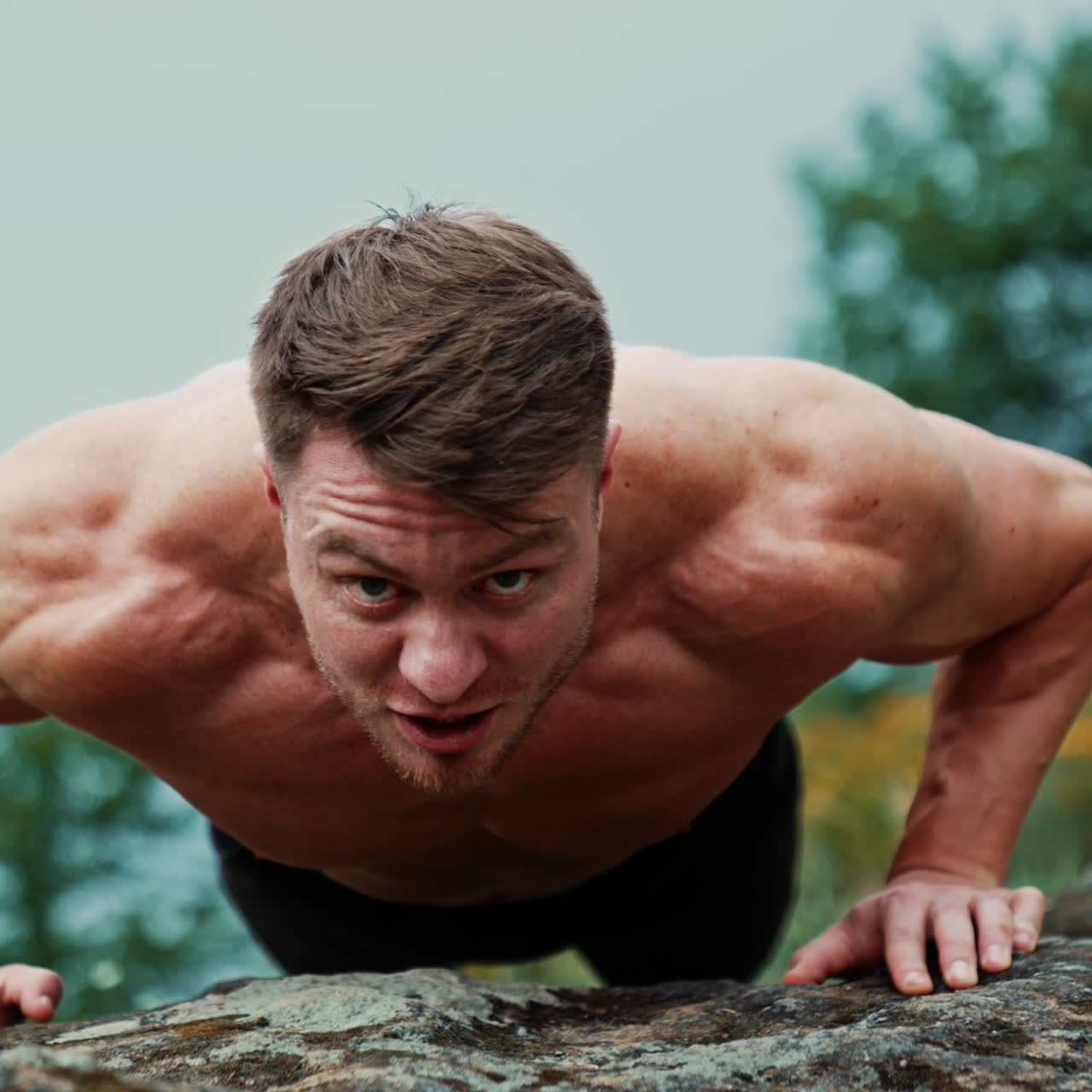 Sportsman smiles doing push-ups. Strong man working out on the rock looking at camera