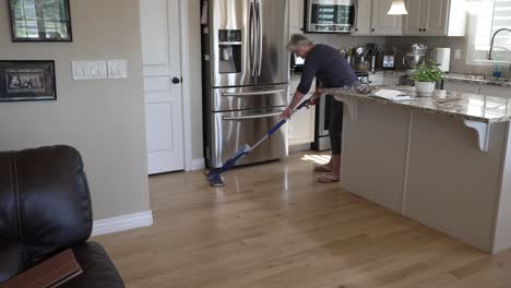 senior woman spray mopping and cleaning her hardwood oak floors - tilt down