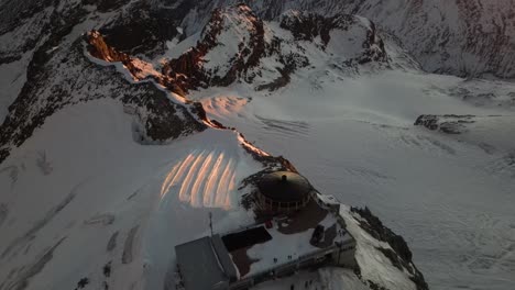 aerial tilt up: mountain ridge on top of the alps, sunrise diffusing an orange light