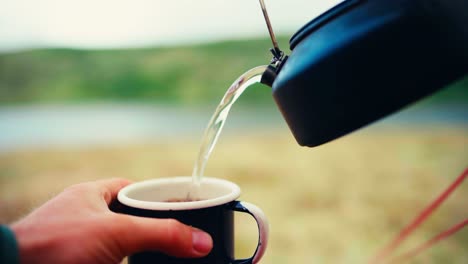 Hand-Gießt-Heißes-Wasser-In-Tasse-Mit-Wasserkocher-Im-Freien-In-Der-Natur---Nahaufnahme