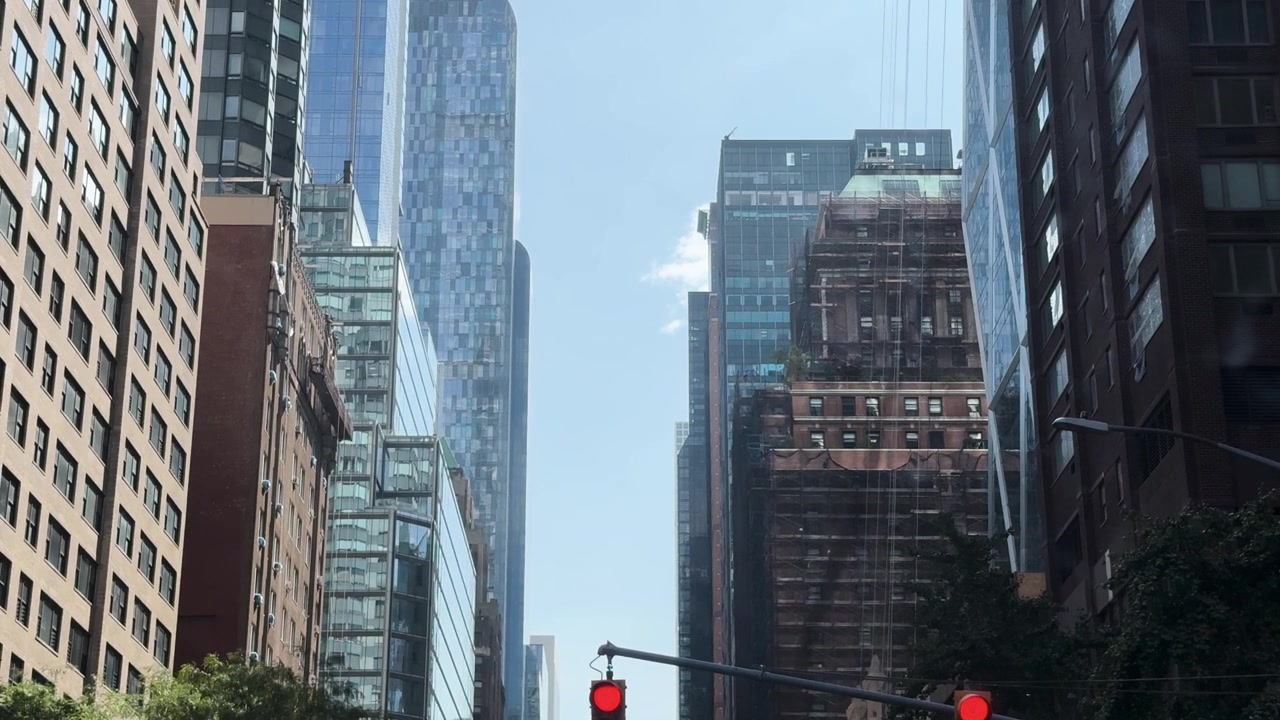 Rascacielos modernos y edificios antiguos bordean una concurrida calle de Manhattan con semáforos