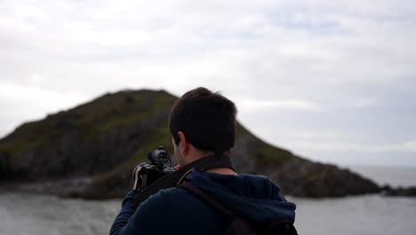 man adjusts his camera settings while filming a video near bracelet bay