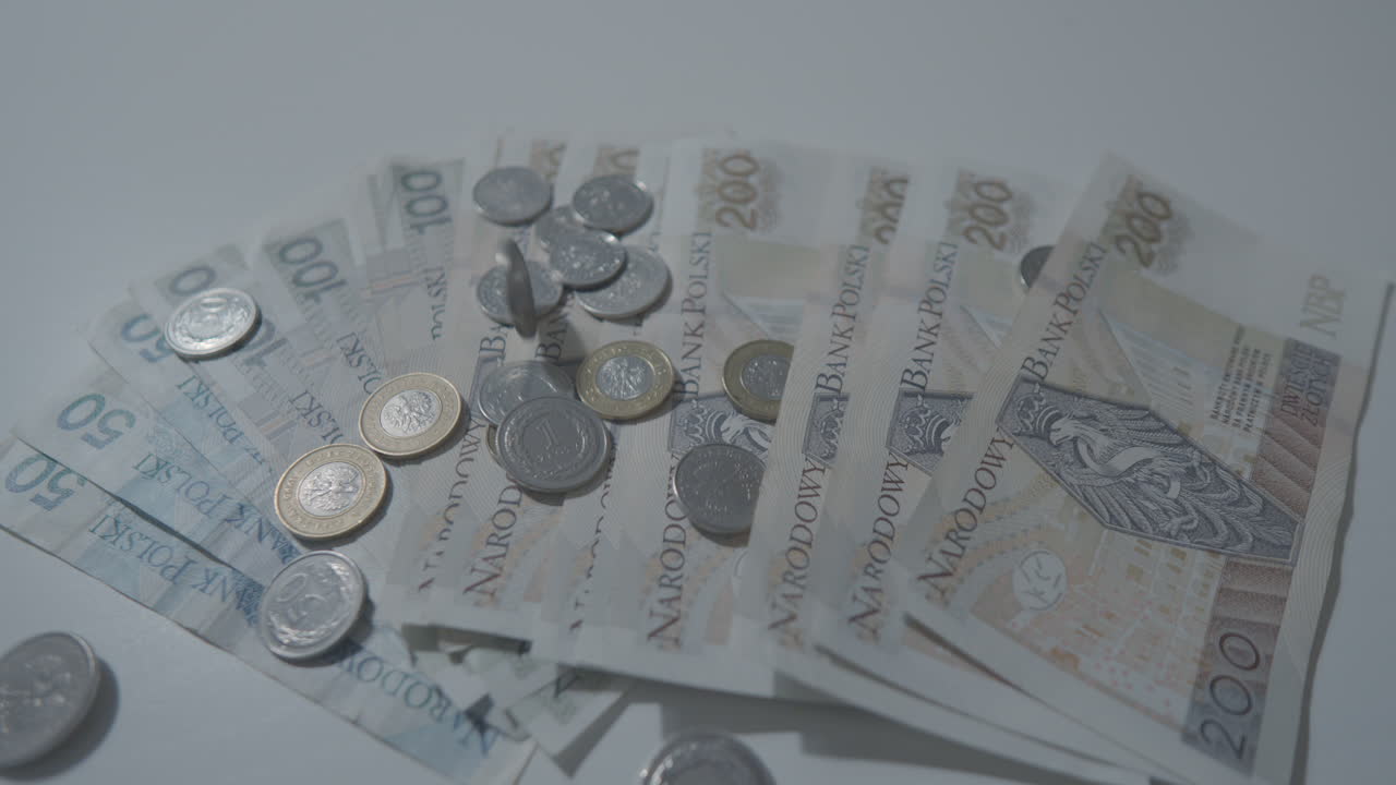 primer plano que muestra la caída de monedas de zloty polaco en billetes en mesa blanca