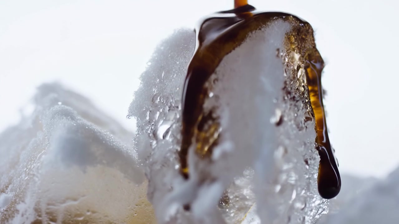 Líquido escuro e viscoso derrama sobre um pico de espuma branca porosa, espalhando uma película úmida e brilhante com gotas alongadas, pérolas, listras reflexivas, textura suave, alto contraste e um impacto visual abstrato e limpo.