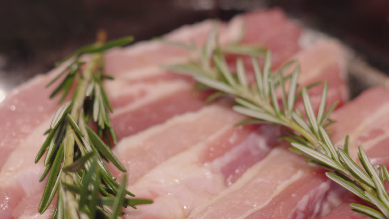 Detalhes em Close-up de Alecrim Fresco Sobre Fatias de Barriga de Porco Crua Fresca Numa Travessa de Vidro Prontas Para Assar No Forno. Saborosa Receita de Jantar À Base de Carne. Vídeo de Comida Mostrando Textura.
