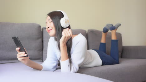 a young pretty woman lying on her stomach is listening and swaying to the music on her smartphone through headphones