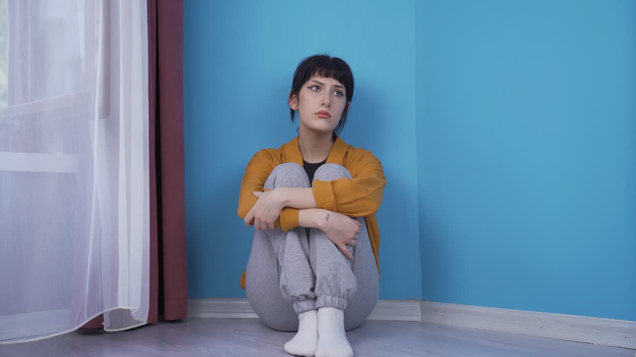 우울한 젊은 여성. 벽  ⁇ 에 앉아 있습니다.