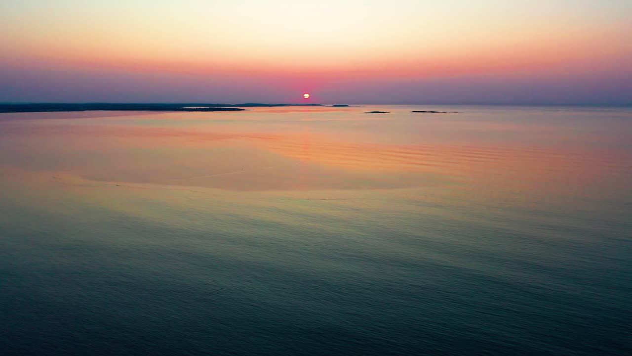 평온한 해가 지는 바다의 끝, 지평선에 있는 작은 섬들 위에서 희미하게 빛나는 태양.
