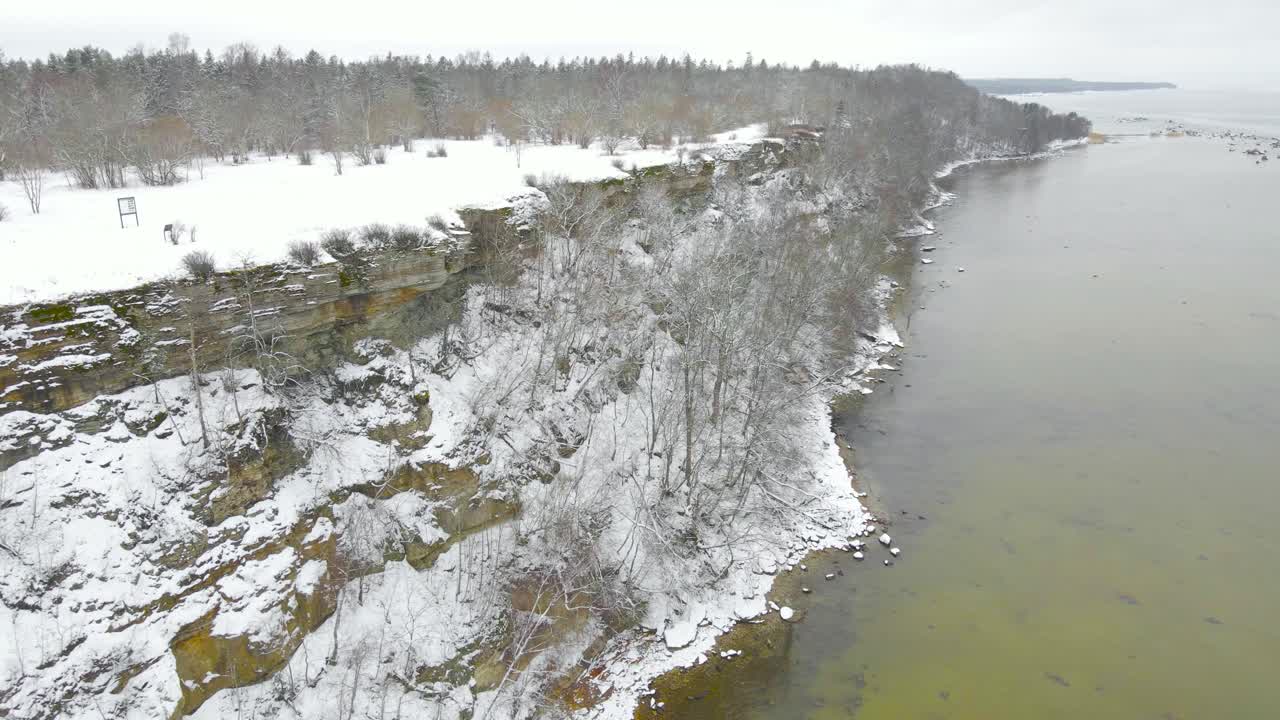 Aerial view of Tabasalu bank cliff, Estonian coast in winter. Beautiful snow covered layered rugged cliffs, trees on the slope of a cliff. High angle view of layered limestone rocks rise above sea